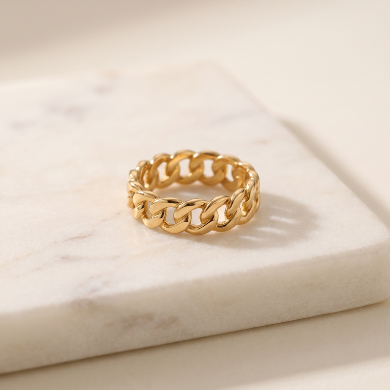 Gold chain link ring in titanium steel, lying on white marble