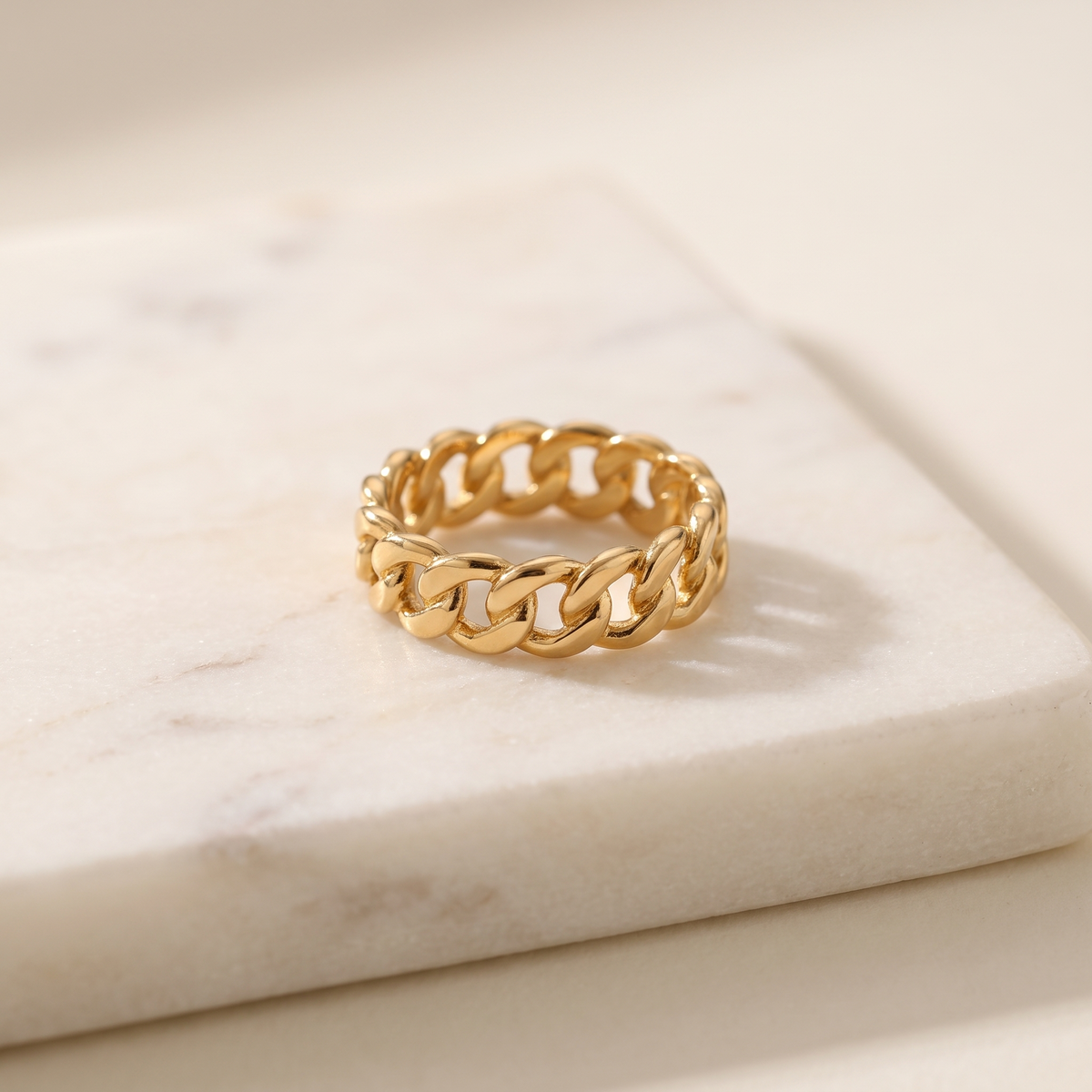 Gold chain link ring in titanium steel, lying on white marble