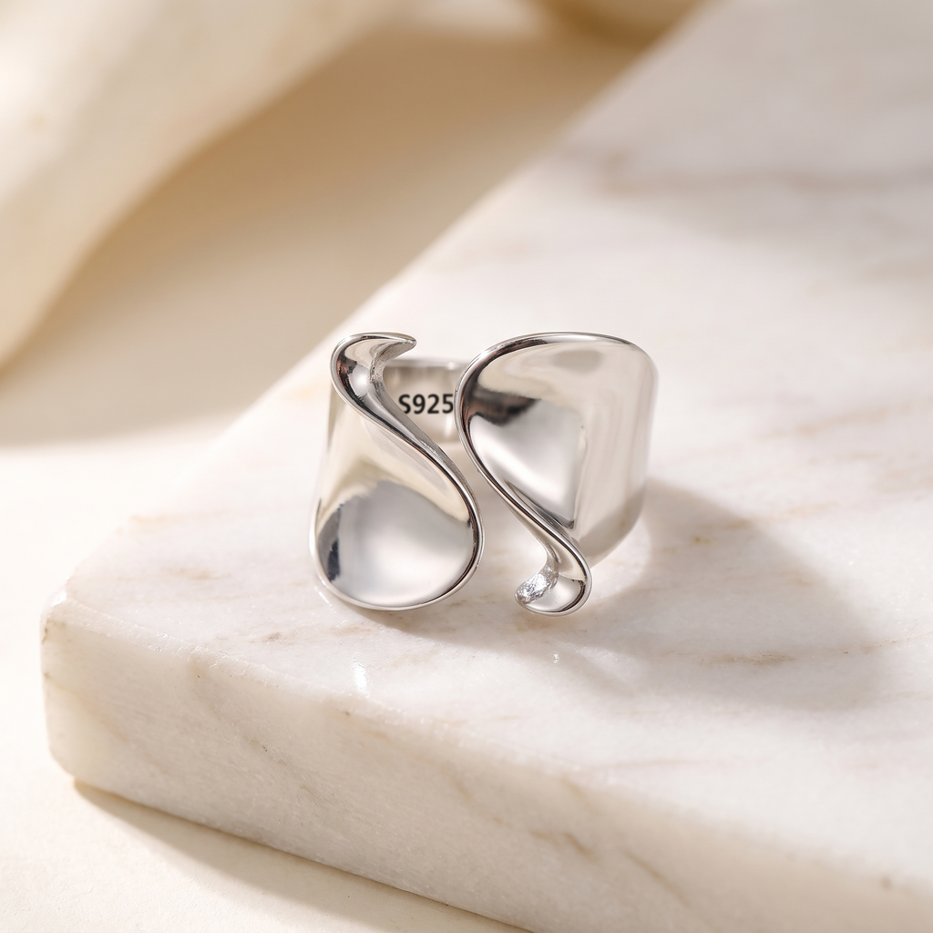 Minimalist geometric open ring in silver stainless steel, lying on white marble