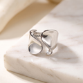 Minimalist geometric open ring in silver stainless steel, lying on white marble