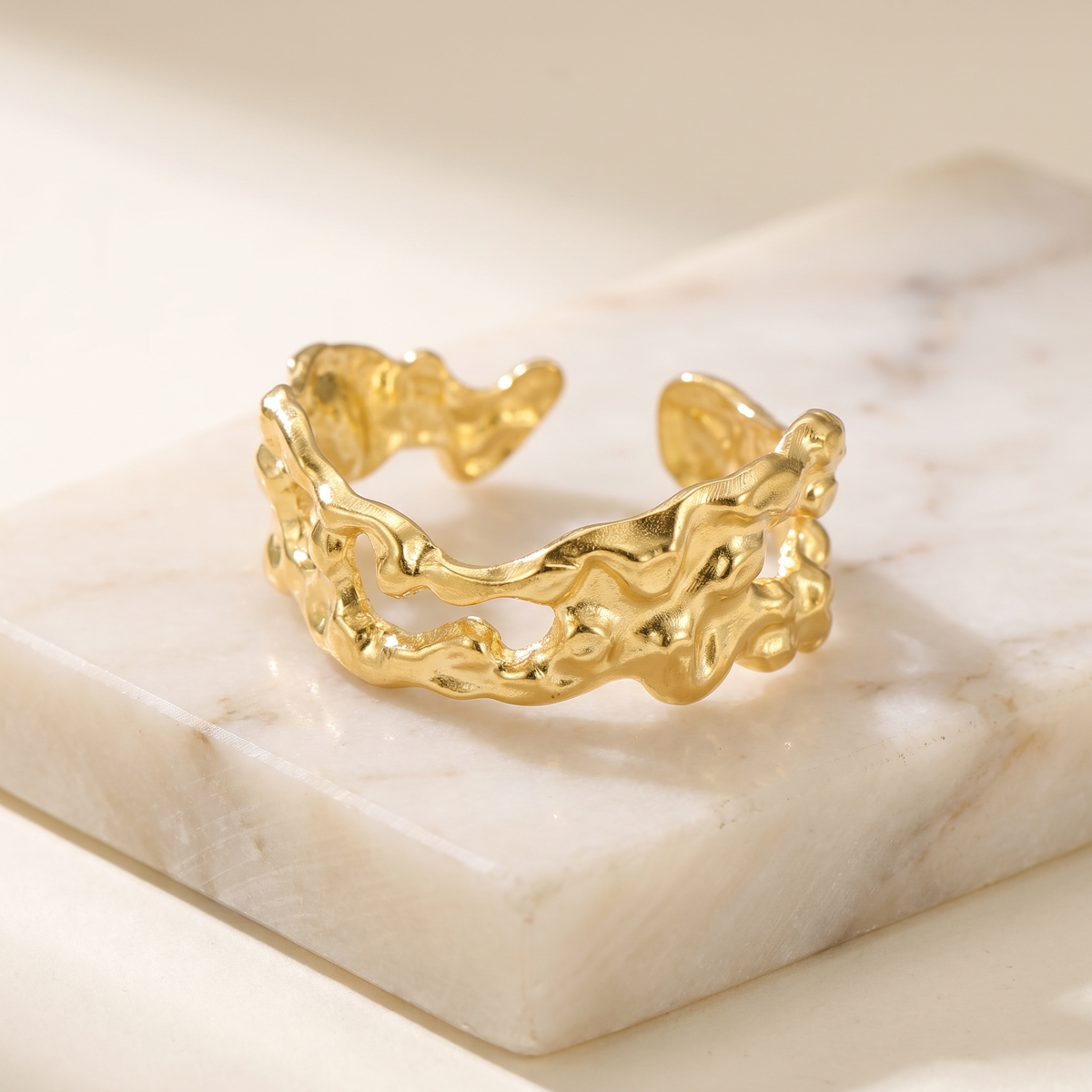 Pleated wide open ring in stainless steel, lying on white marble