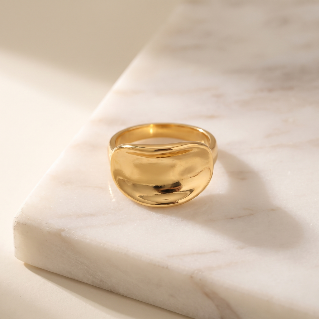 Ribbon twist ring in gold tone, lying on white marble