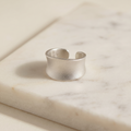 Frosted matte wide band ring in stainless steel, lying on white marble