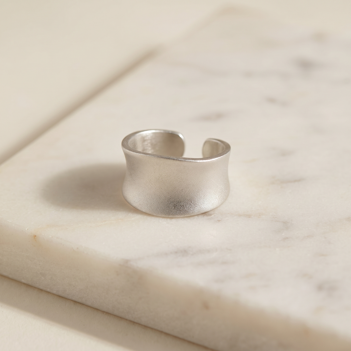 Frosted matte wide band ring in stainless steel, lying on white marble