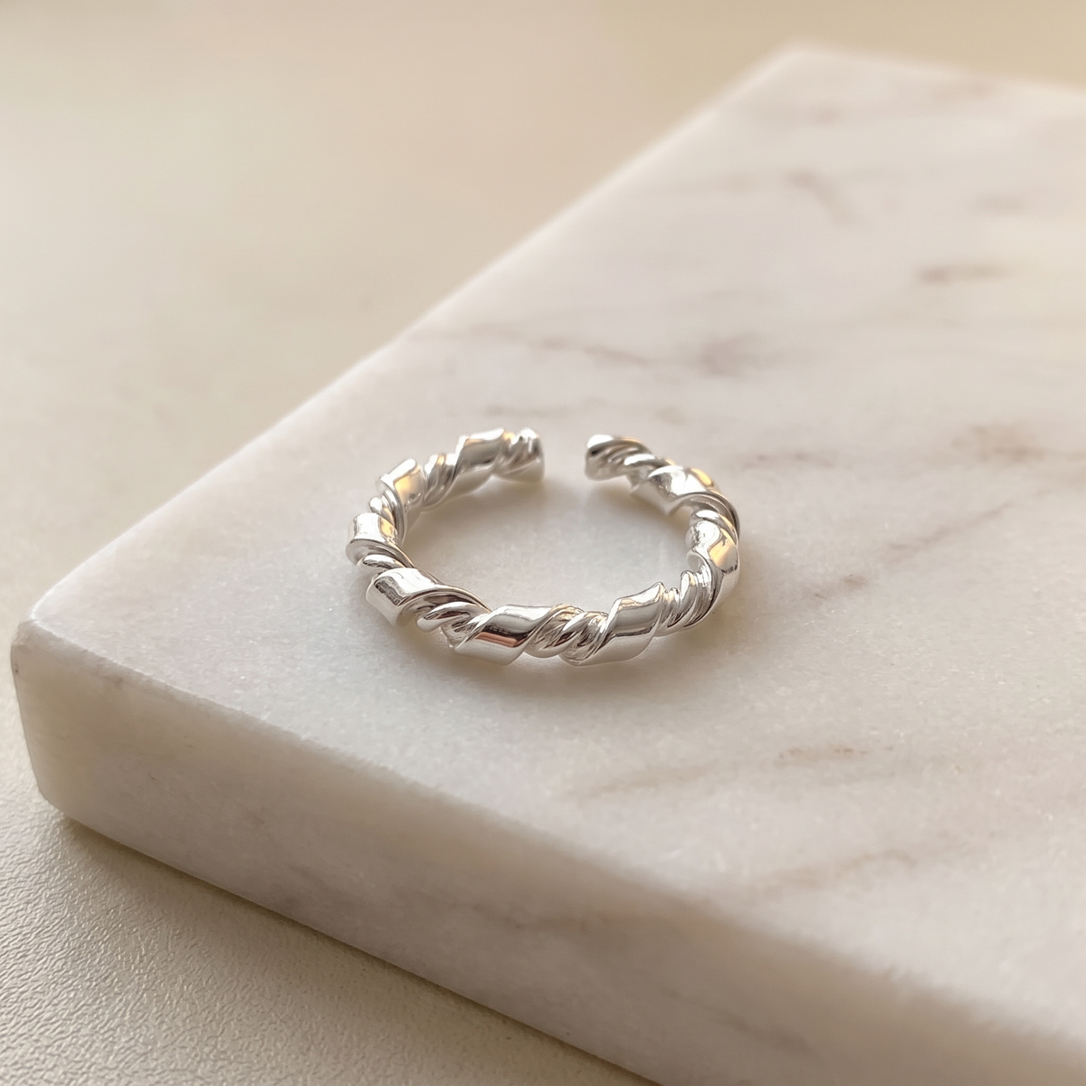 Adjustable sterling silver knot ring, lying on white marble