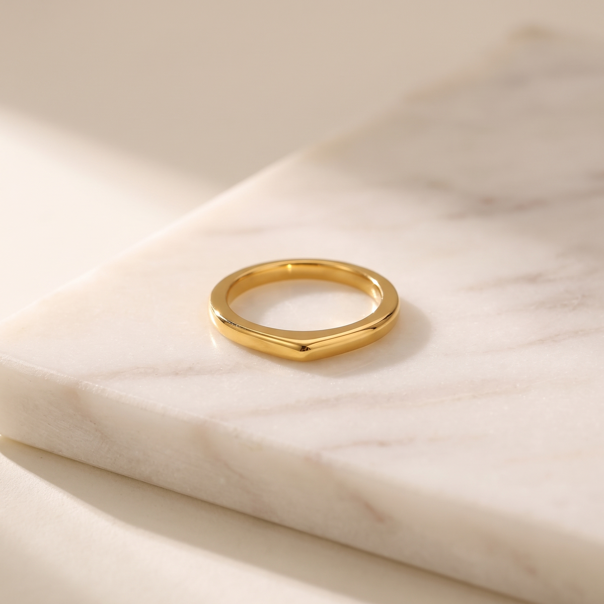Geometric gold stacking ring in stainless steel, lying on white marble