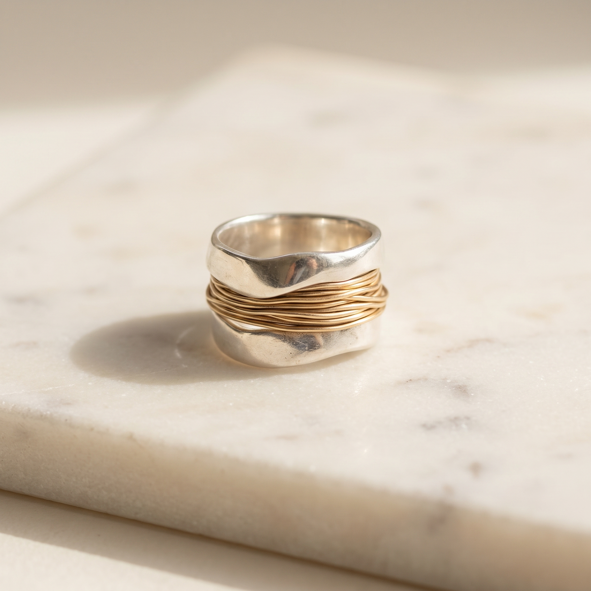 Two-tone gold and silver wide band ring, lying on white marble
