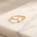 Gold initial letter ring set with zircon, lying on white marble