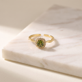 Olive green zircon open ring in gold, lying on white marble