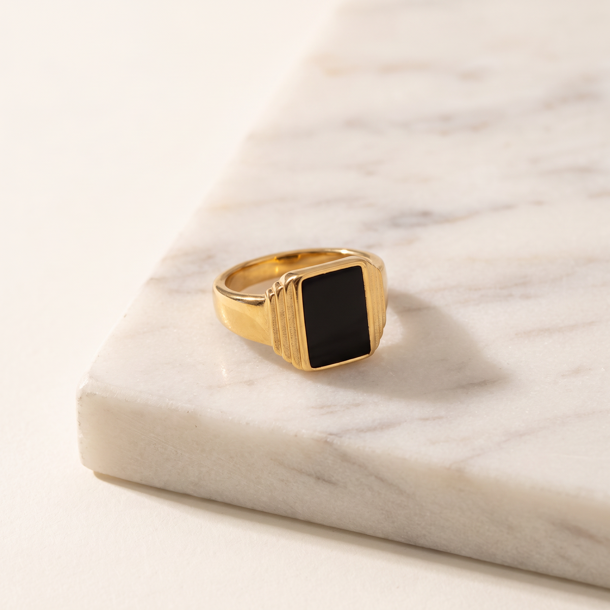 Black onyx square signet ring in 18K gold plating, lying on white marble