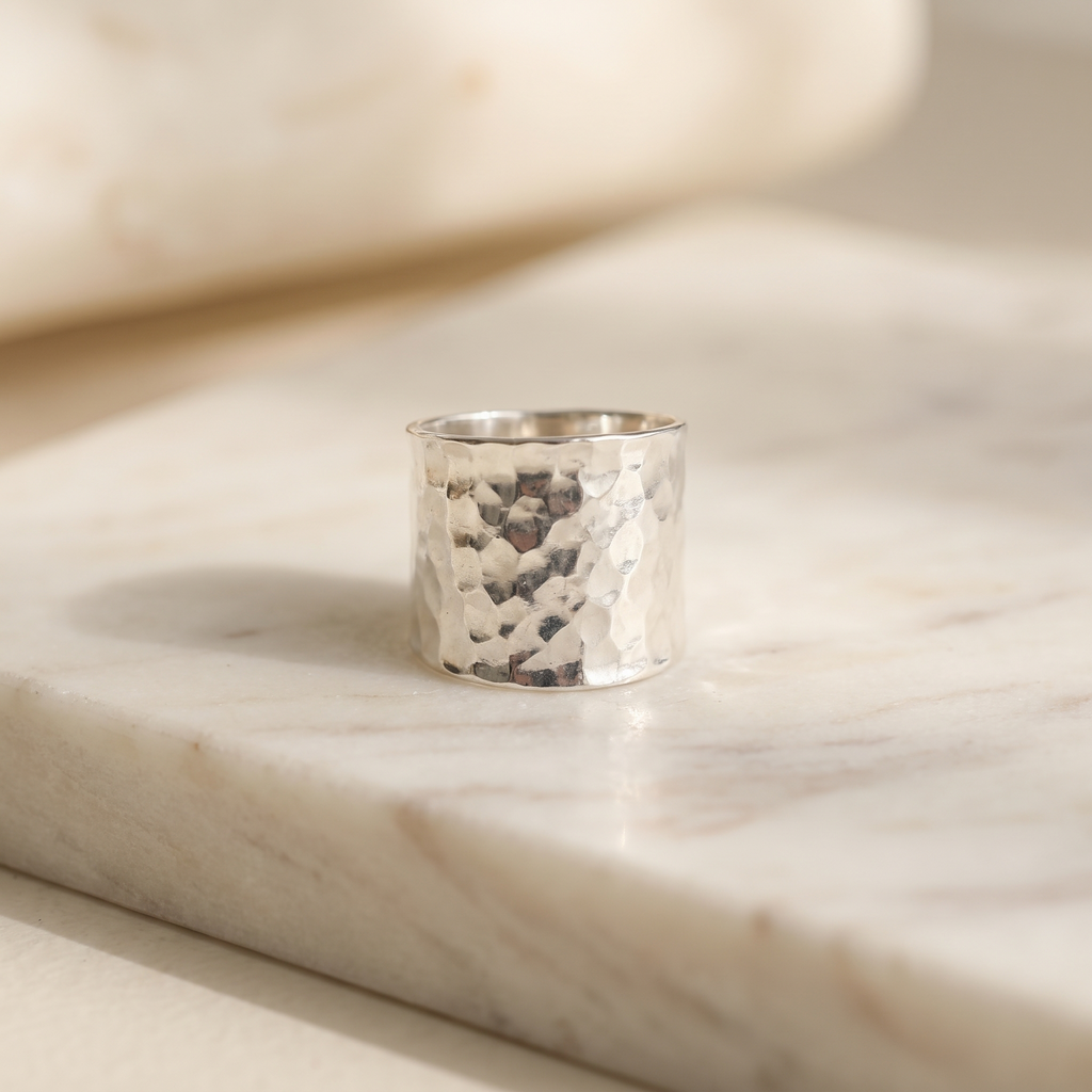 Hand-hammered solid sterling silver wide band ring, lying on white marble