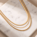 Layered gold snake chain necklace on white marble
