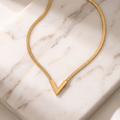 Gold V-shaped snake chain necklace on white marble