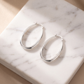 Oval sculpted hoop earrings on white marble