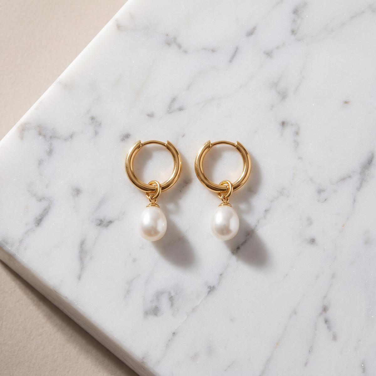 Gold teardrop pearl earrings on white marble