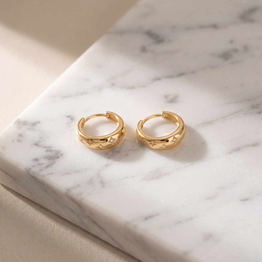 Gold star charm hoop earrings on white marble