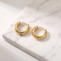 Textured gold huggie hoop earrings on white marble