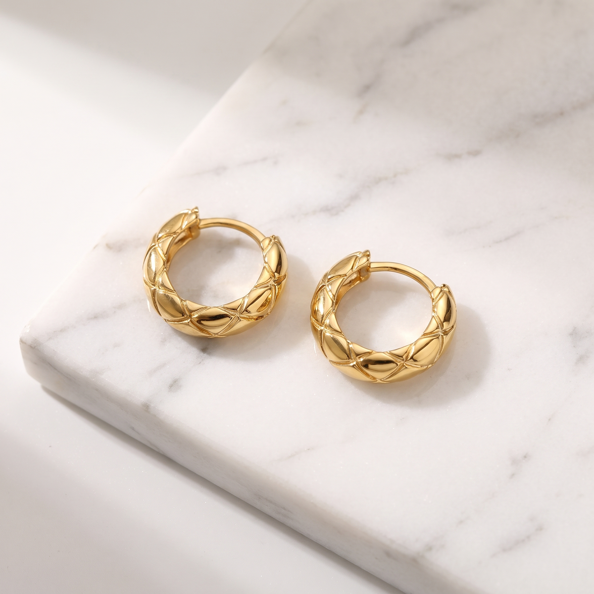 Textured gold huggie hoop earrings on white marble
