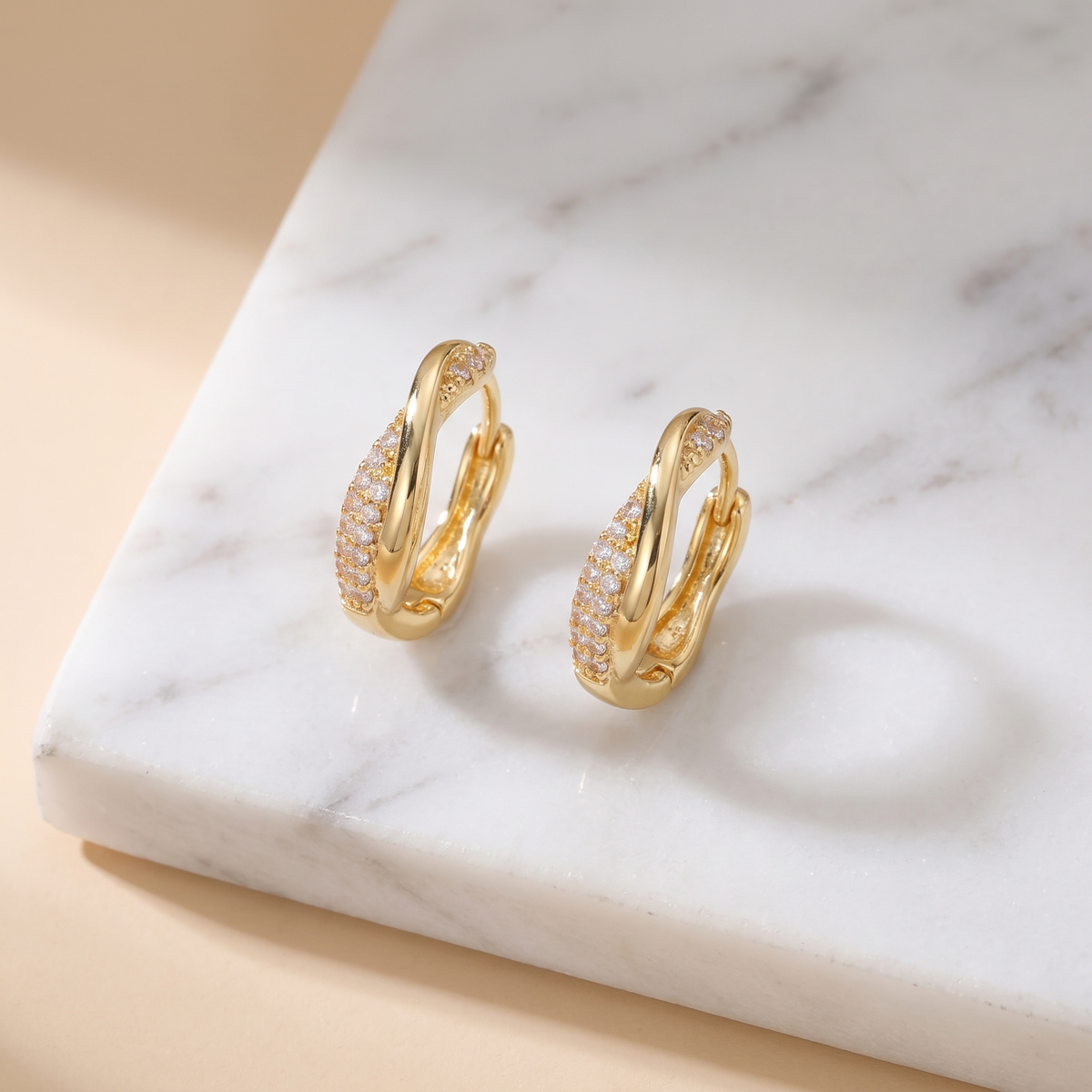Twisted pave gold huggie hoop earrings on white marble