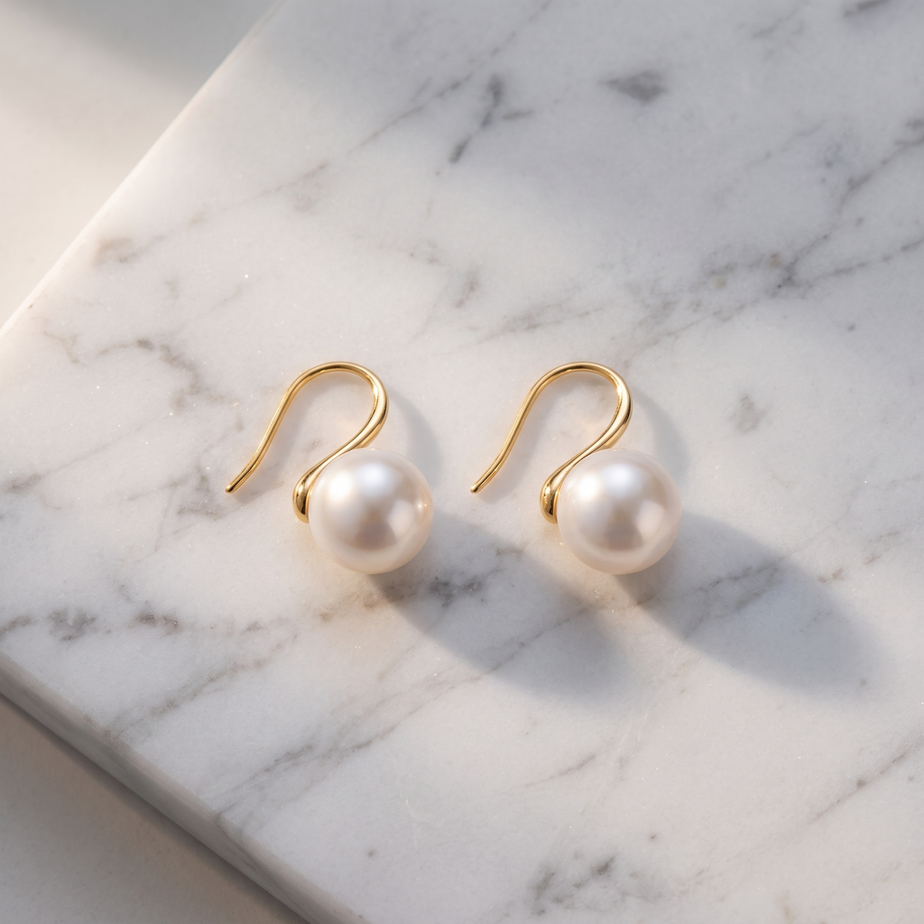 Gold pearl hook earrings on white marble
