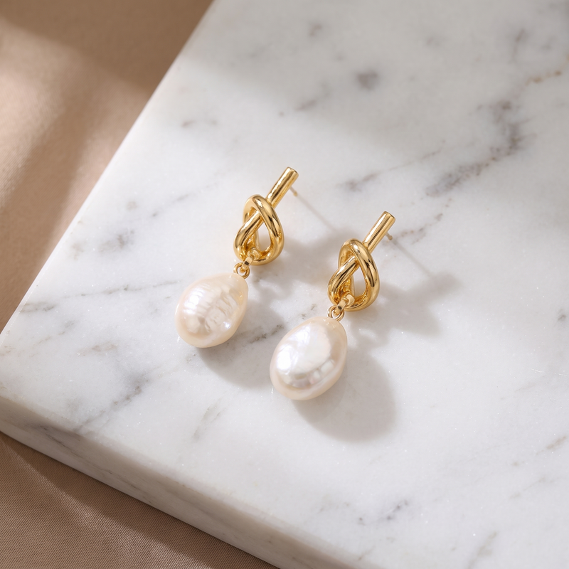Baroque pearl knot drop earrings in gold on white marble