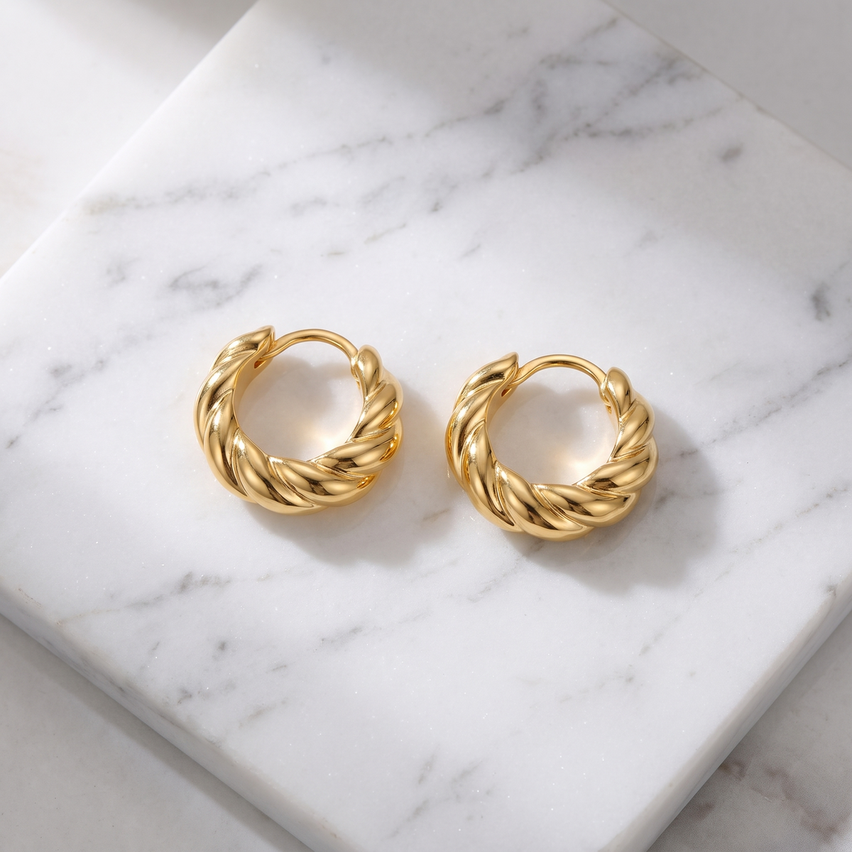 Croissant twist gold hoop earrings on white marble